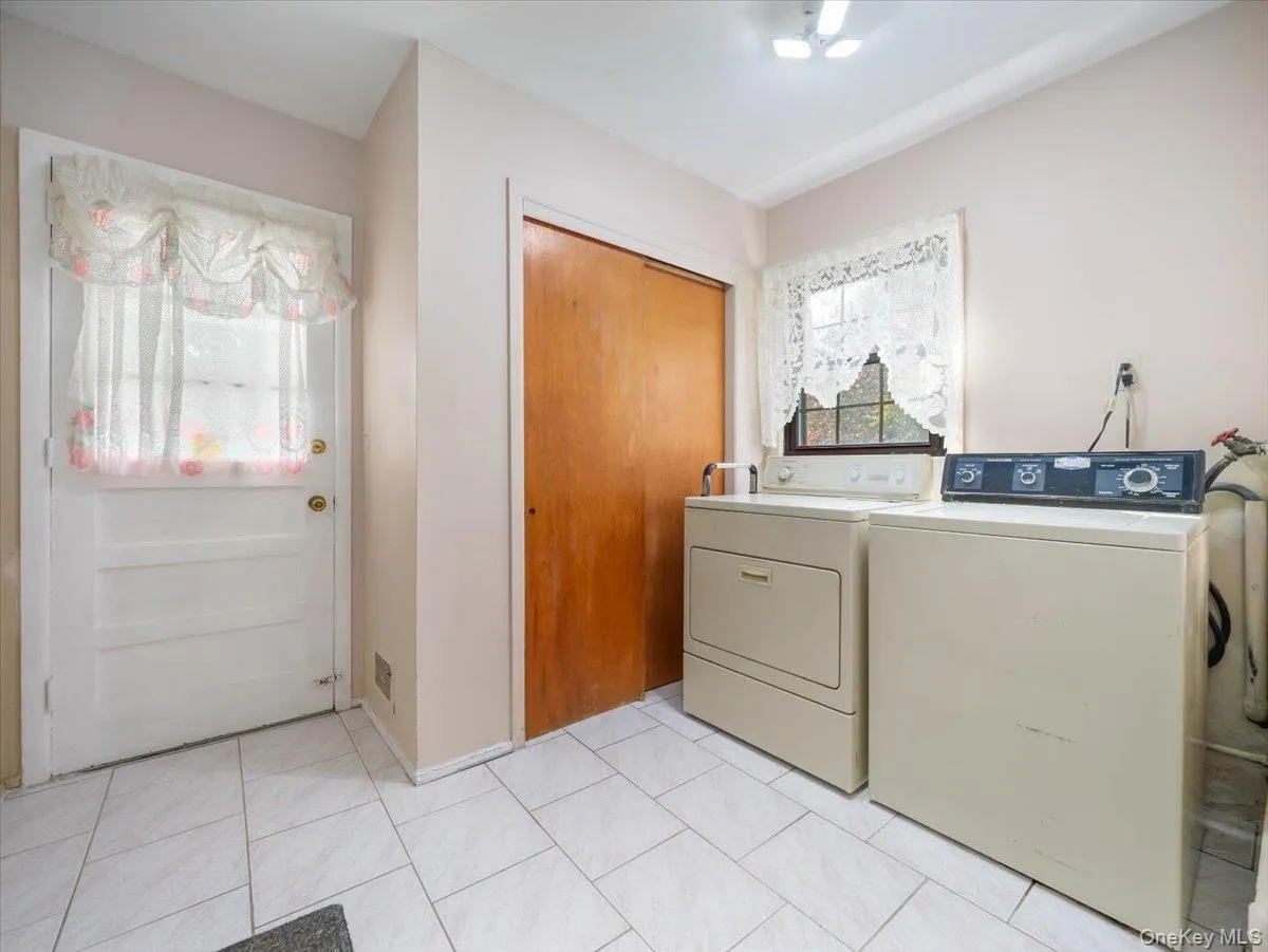 Laundry room featuring white tile flooring, wood-finish closet doors, and an exterior door with inset glass Laundry room featuring white tile flooring, wood-finish closet doors, and an exterior door with inset glass