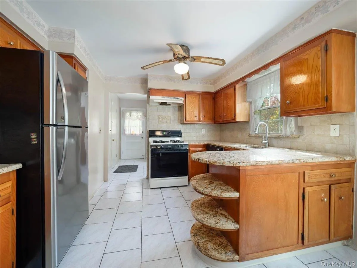 Kitchen featuring wood cabinetry, natural stone countertops with integrated open shelving, tile flooring, and stainless steel appliances Kitchen featuring wood cabinetry, natural stone countertops with integrated open shelving, tile flooring, and stainless steel appliances