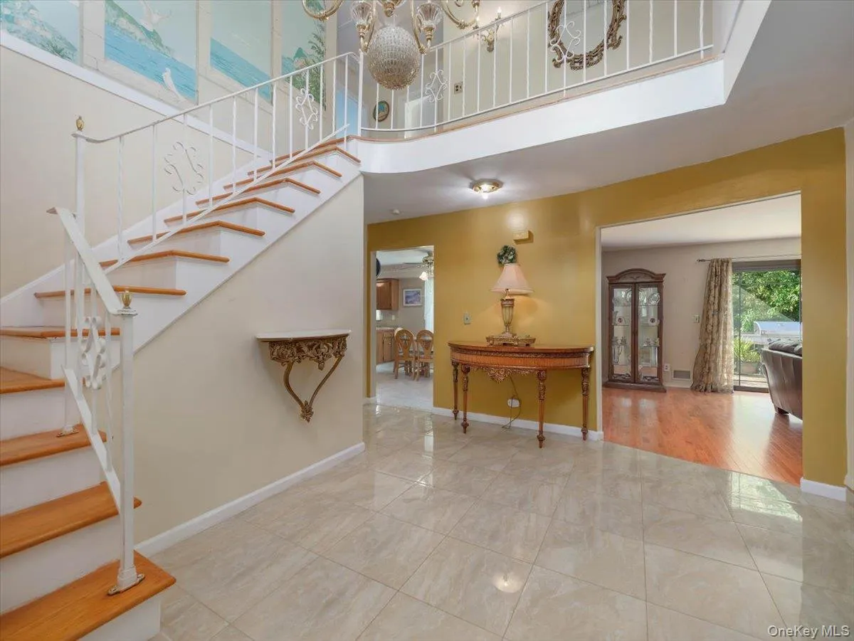 Foyer featuring large-format tile flooring, a curved staircase with white metal railings, wood-finish stair treads, and a crystal-style chandelier Foyer featuring large-format tile flooring, a curved staircase with white metal railings, wood-finish stair treads, and a crystal-style chandelier