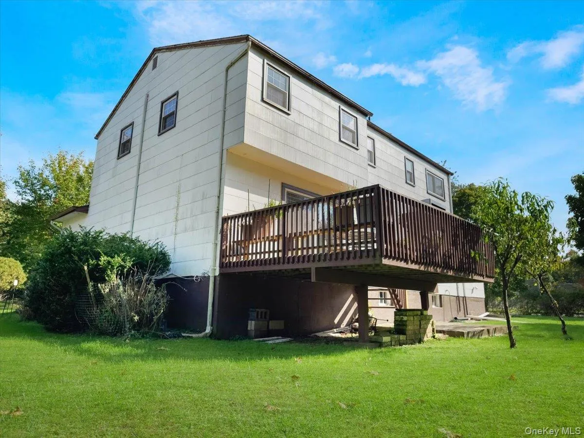 Rear exterior featuring vertical siding, a raised wood deck with balustrades, a stone retaining wall, and a large grassy lot Rear exterior featuring vertical siding, a raised wood deck with balustrades, a stone retaining wall, and a large grassy lot