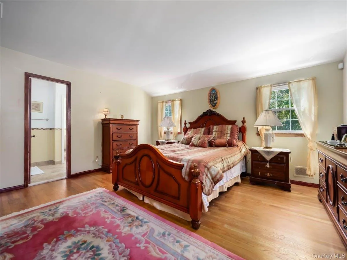 Bedroom featuring wood-finish flooring, dual windows, and an arched entryway Bedroom featuring wood-finish flooring, dual windows, and an arched entryway