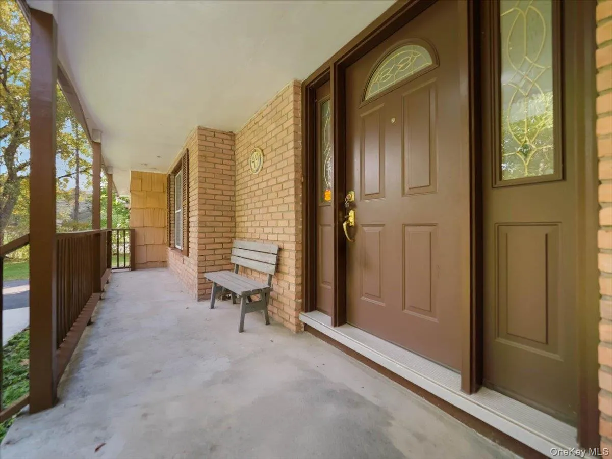 Covered front porch featuring a brick exterior, solid wood-finish entry door with leaded glass inserts, and wood railing Covered front porch featuring a brick exterior, solid wood-finish entry door with leaded glass inserts, and wood railing