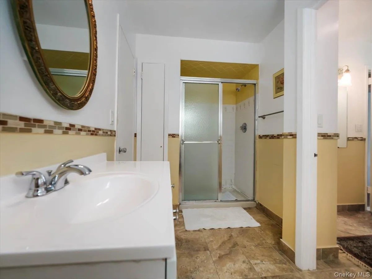 Bathroom featuring a vanity with a white integrated sink, walk-in shower with a sliding glass door, decorative tile backsplash, and tile flooring Bathroom featuring a vanity with a white integrated sink, walk-in shower with a sliding glass door, decorative tile backsplash, and tile flooring