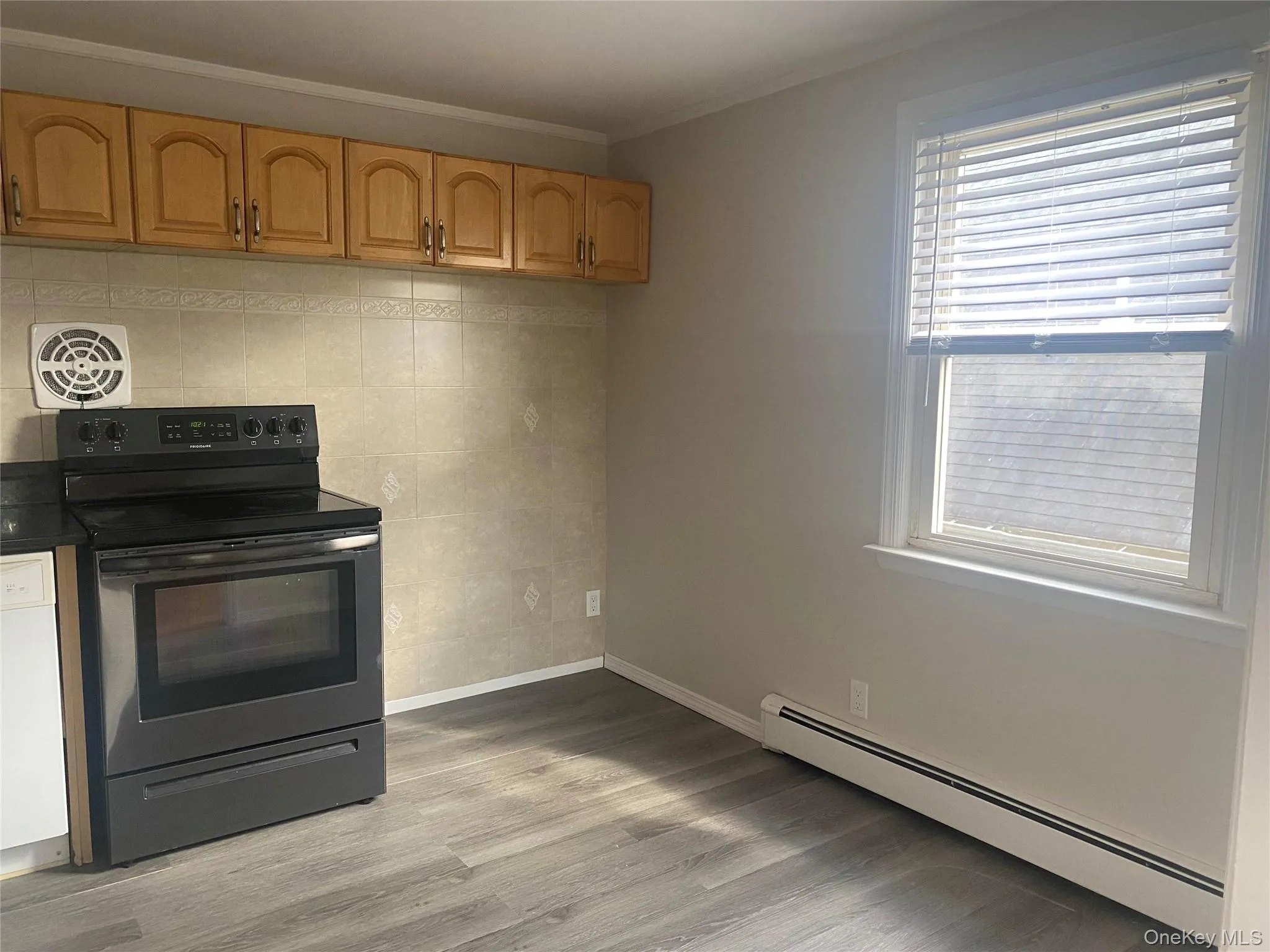 Upper wood-finish cabinetry, tile backsplash, black electric range ,new flooring, and a single window with blinds Upper wood-finish cabinetry, tile backsplash, black electric range ,new flooring, and a single window with blinds