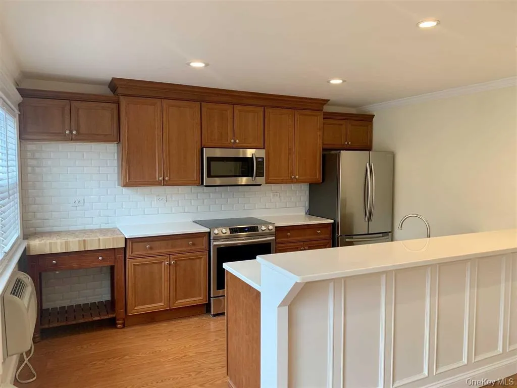 Kitchen featuring appliances with stainless steel finishes, brown cabinets, crown molding, light countertops, and decorative backsplash Kitchen featuring appliances with stainless steel finishes, brown cabinets, crown molding, light countertops, and decorative backsplash