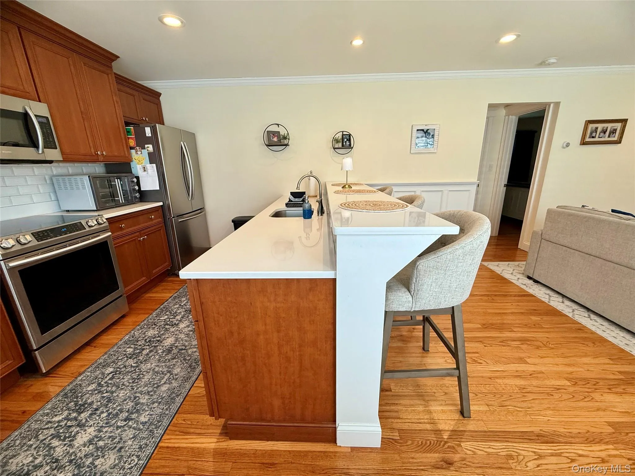 Kitchen featuring appliances with stainless steel finishes, crown molding, a breakfast bar, light wood-type flooring, and tasteful backsplash Kitchen featuring appliances with stainless steel finishes, crown molding, a breakfast bar, light wood-type flooring, and tasteful backsplash