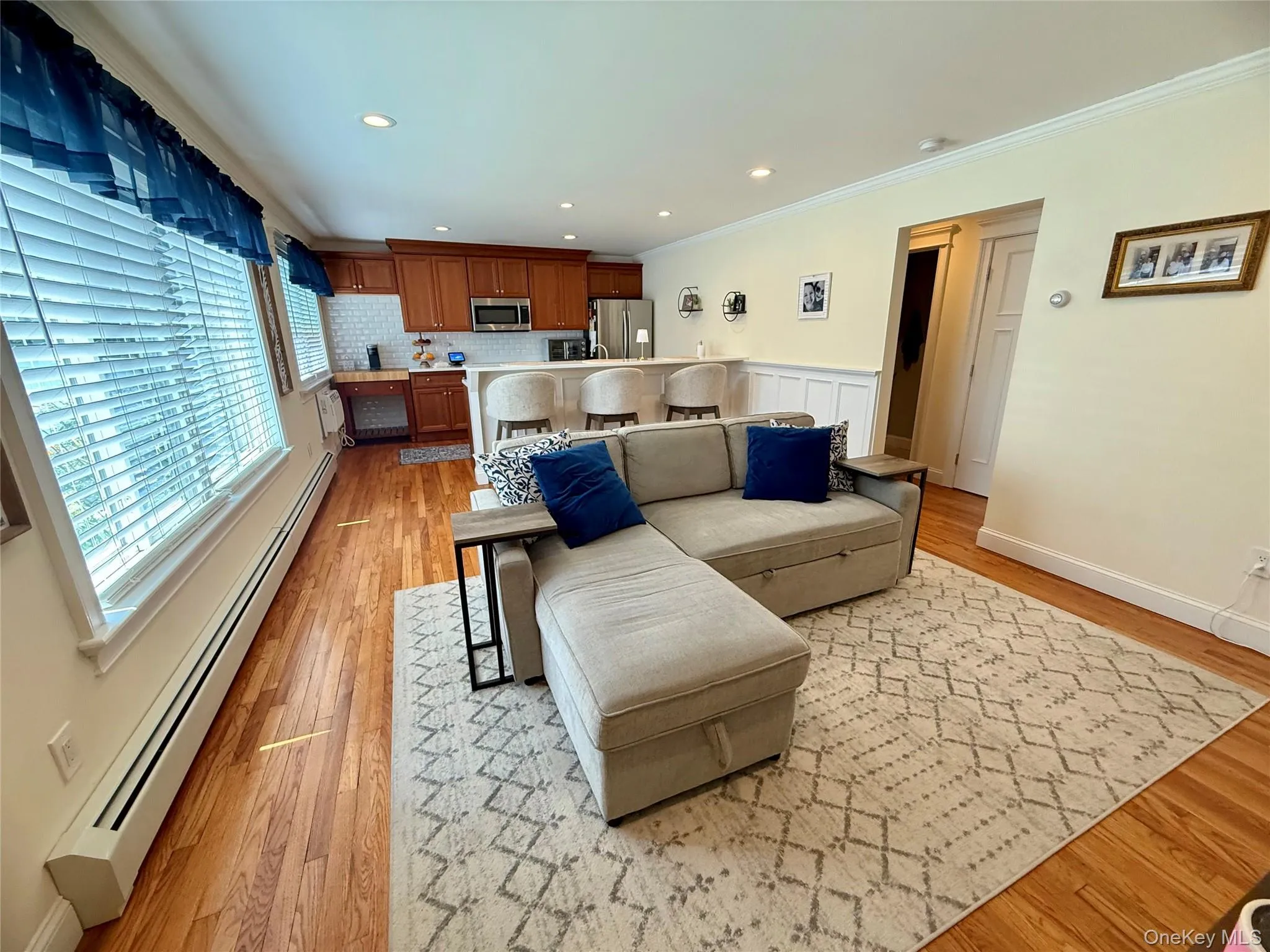 Living area with a baseboard heating unit, healthy amount of natural light, crown molding, light wood-type flooring, and a wainscoted wall Living area with a baseboard heating unit, healthy amount of natural light, crown molding, light wood-type flooring, and a wainscoted wall