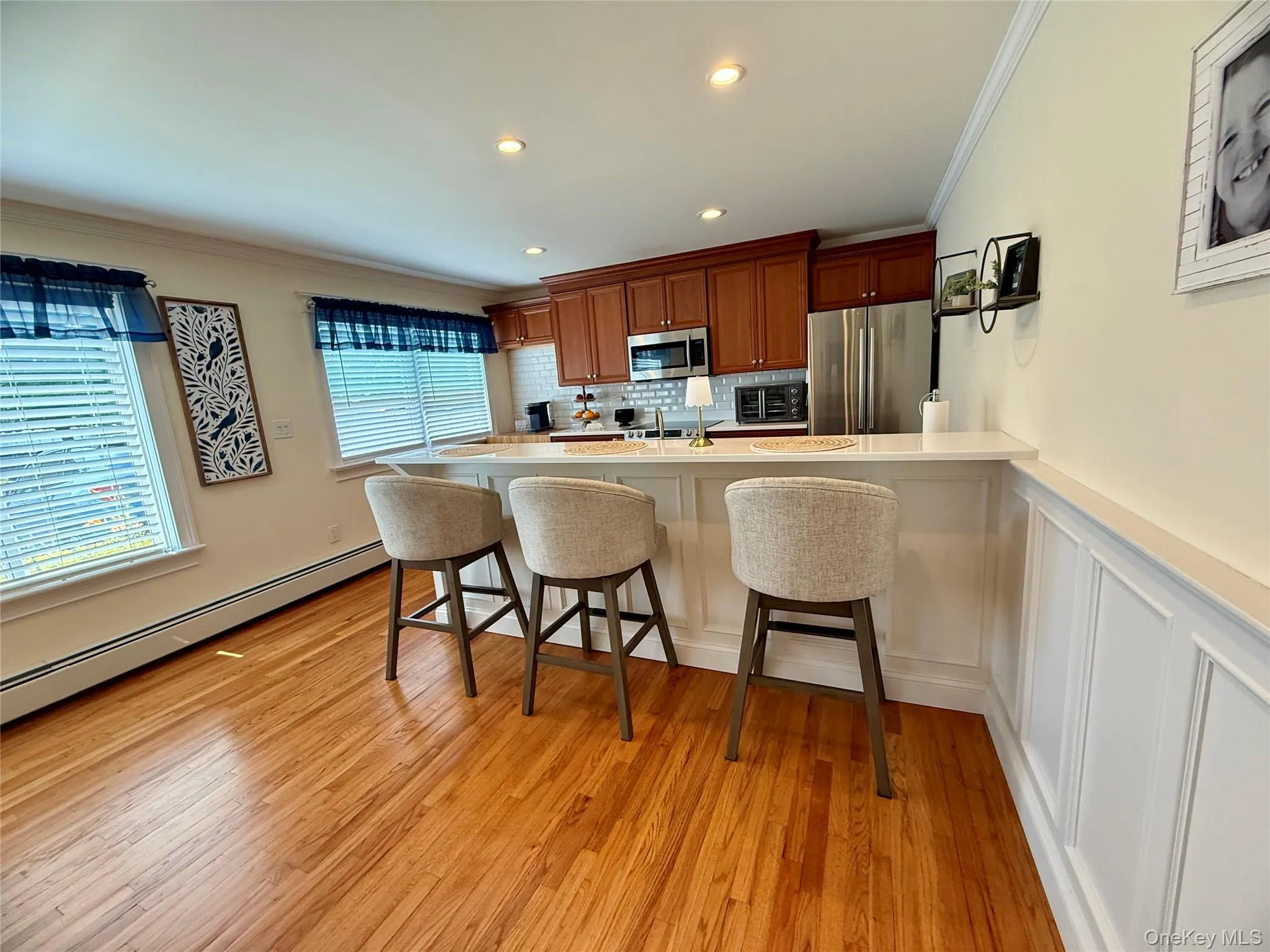 Kitchen featuring stainless steel appliances, crown molding, a kitchen breakfast bar, brown cabinets, and light countertops Kitchen featuring stainless steel appliances, crown molding, a kitchen breakfast bar, brown cabinets, and light countertops
