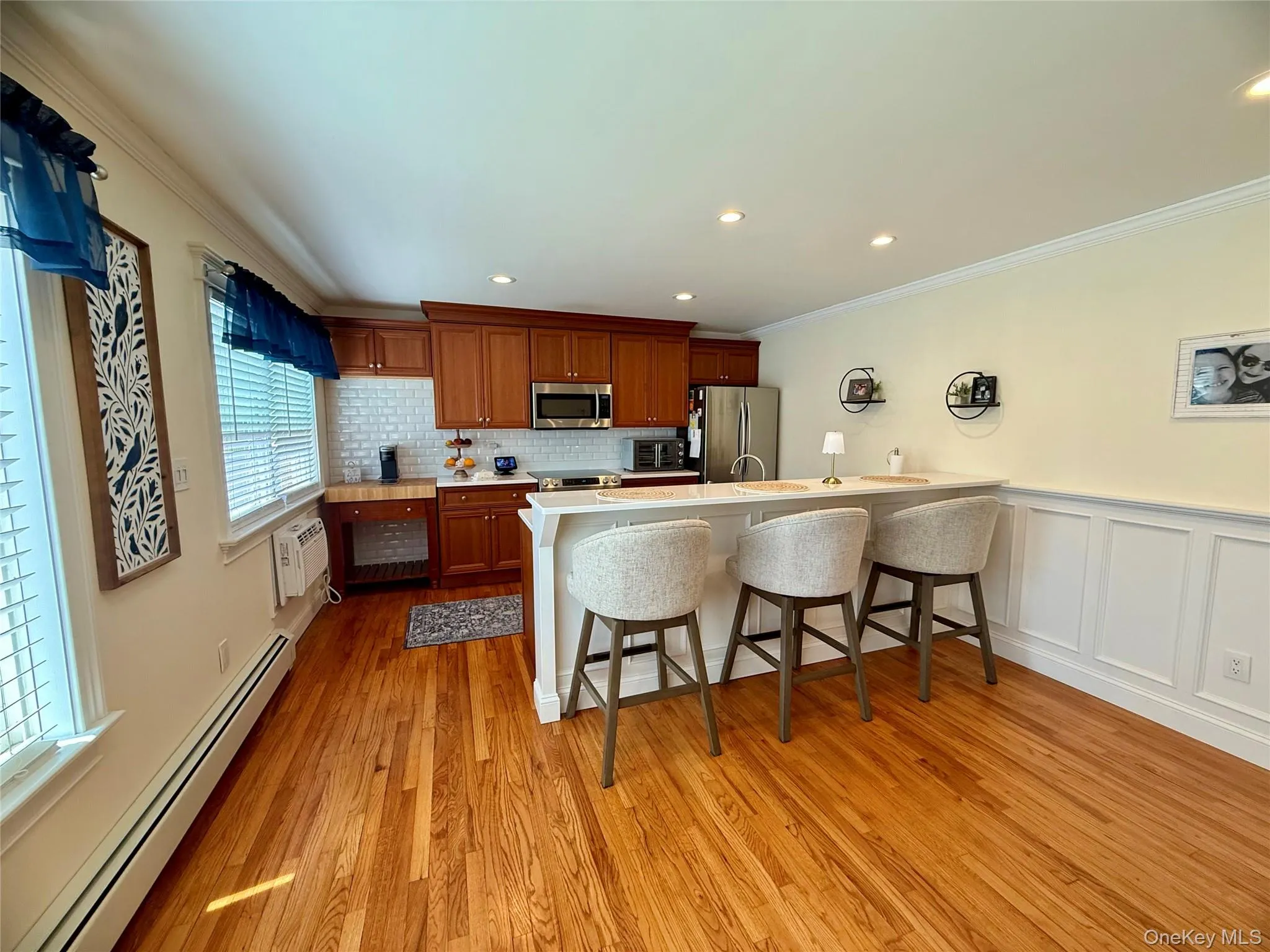 Kitchen with a baseboard radiator, appliances with stainless steel finishes, a kitchen breakfast bar, crown molding, and light countertops Kitchen with a baseboard radiator, appliances with stainless steel finishes, a kitchen breakfast bar, crown molding, and light countertops