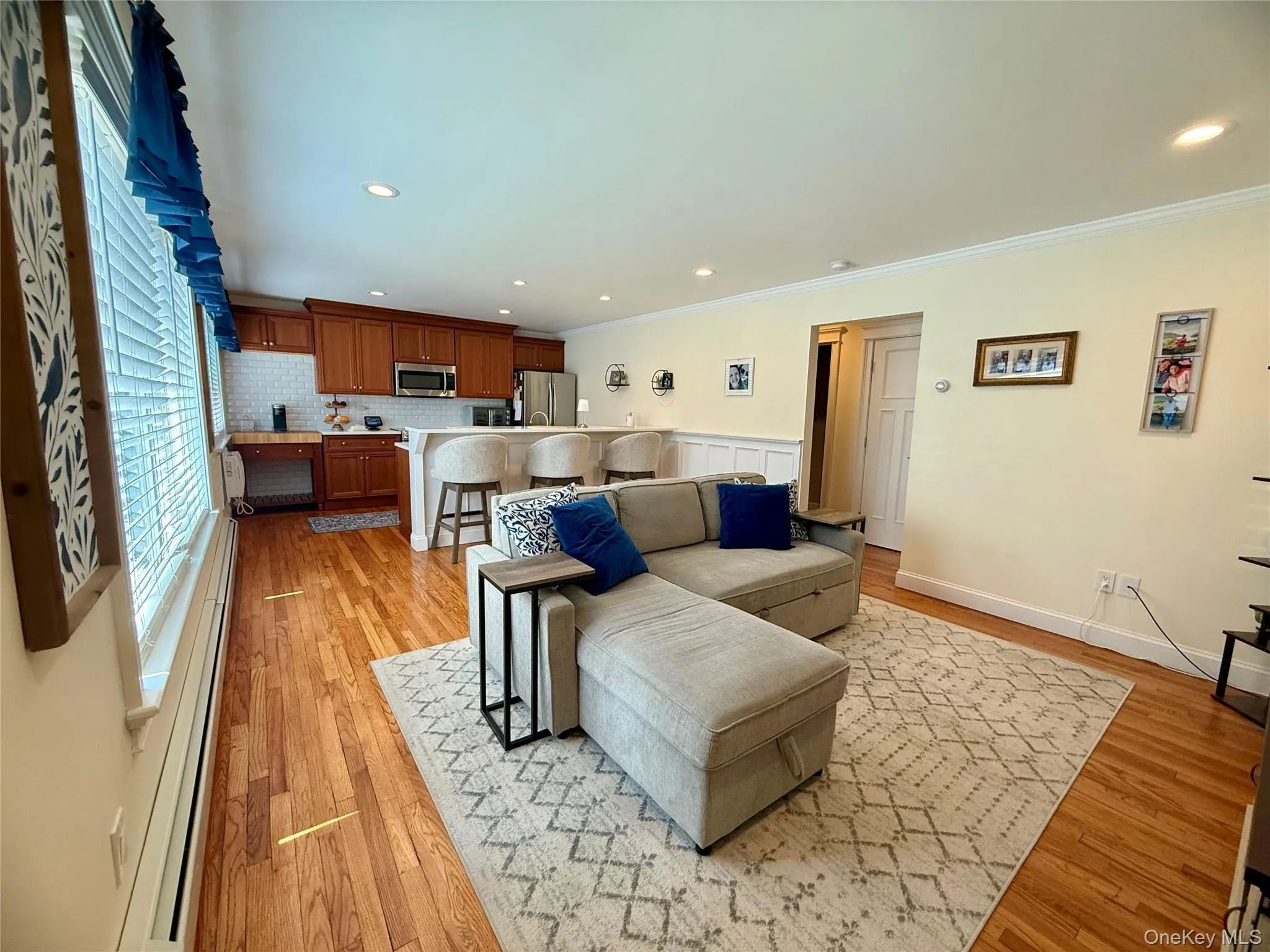 Living area with baseboard heating, ornamental molding, light wood-style flooring, and recessed lighting Living area with baseboard heating, ornamental molding, light wood-style flooring, and recessed lighting