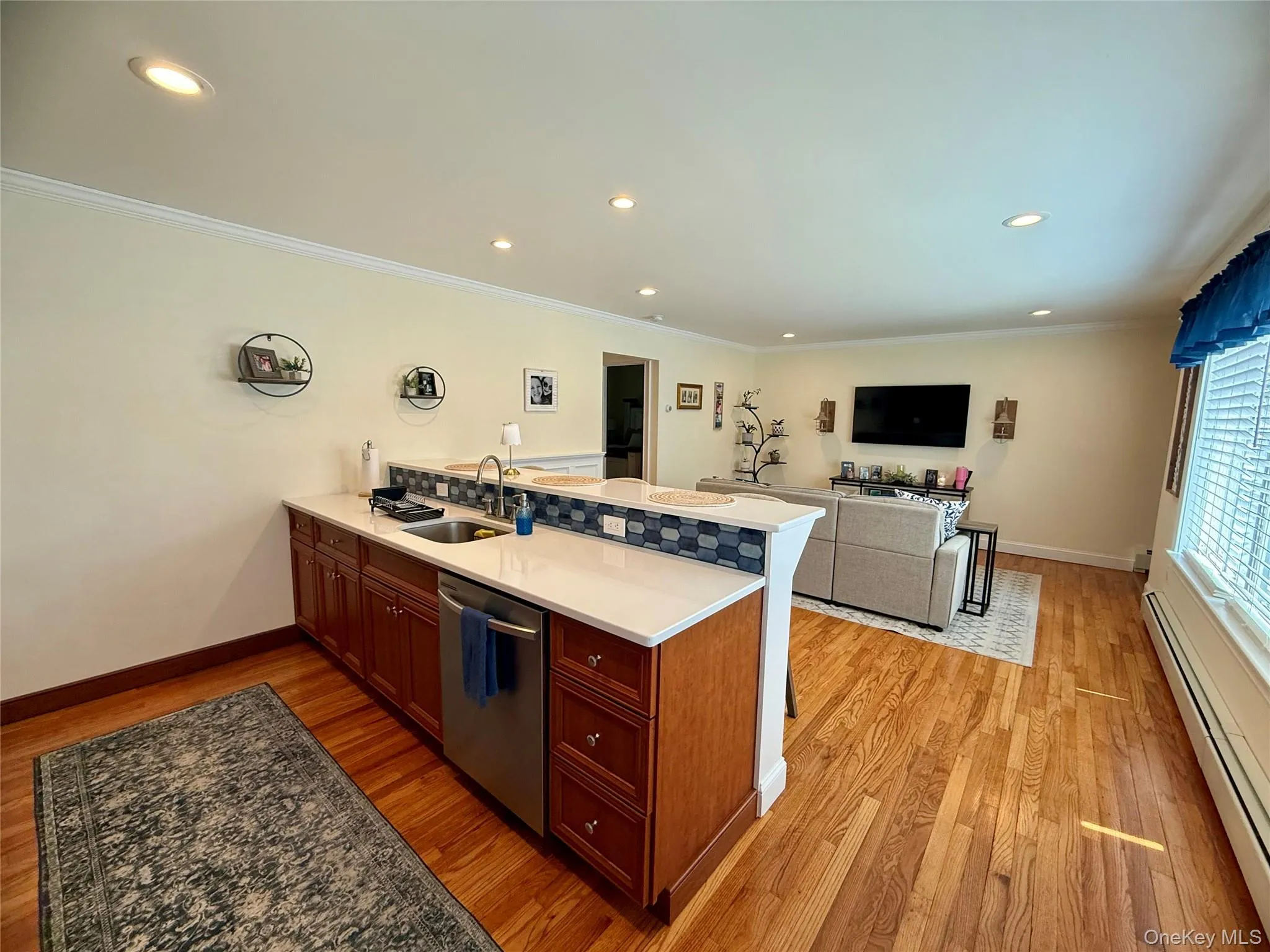 Kitchen with stainless steel dishwasher, a peninsula, a baseboard heating unit, light wood-style floors, and ornamental molding Kitchen with stainless steel dishwasher, a peninsula, a baseboard heating unit, light wood-style floors, and ornamental molding