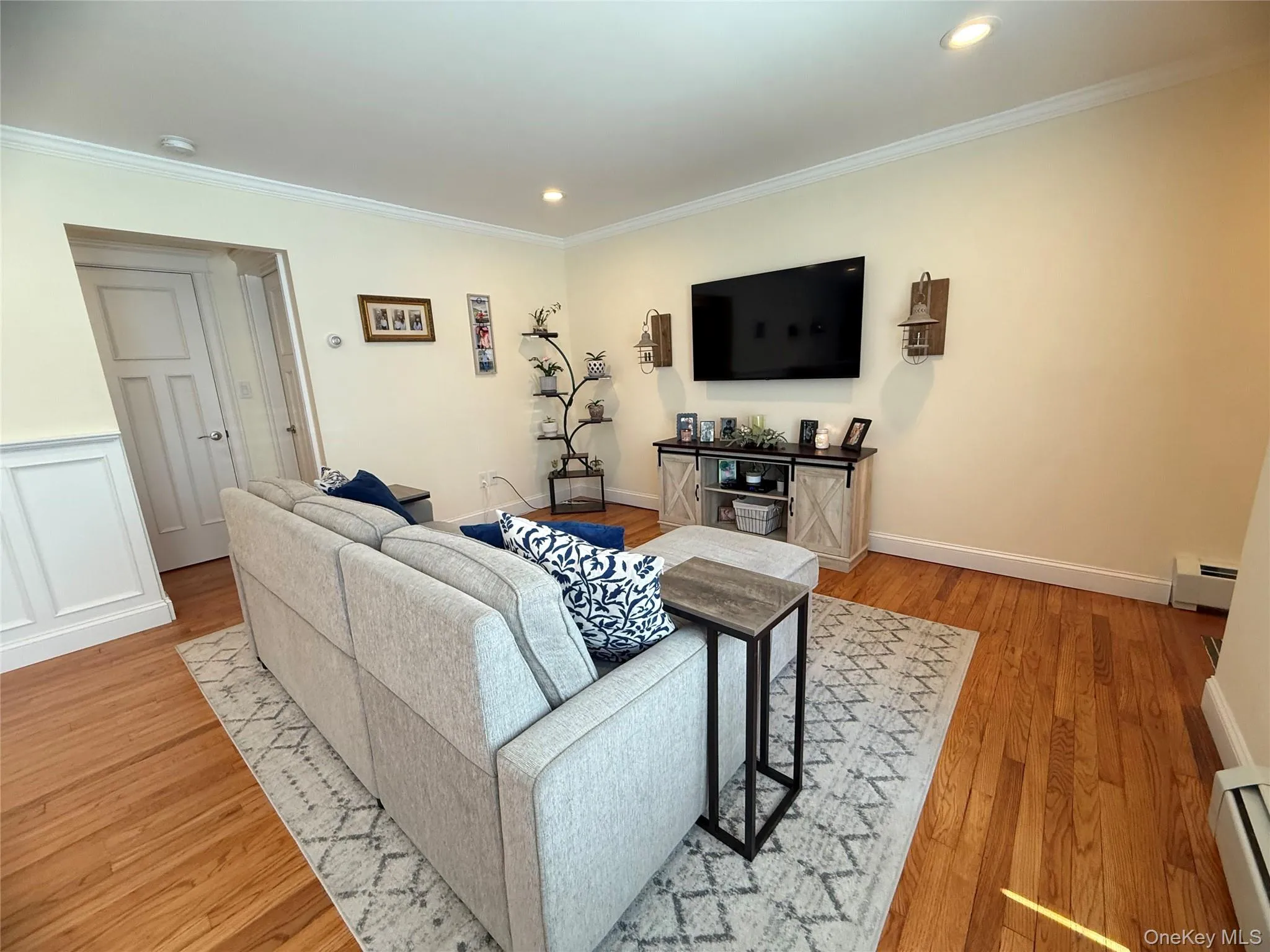 Living room with a baseboard radiator, ornamental molding, light wood-type flooring, and recessed lighting Living room with a baseboard radiator, ornamental molding, light wood-type flooring, and recessed lighting