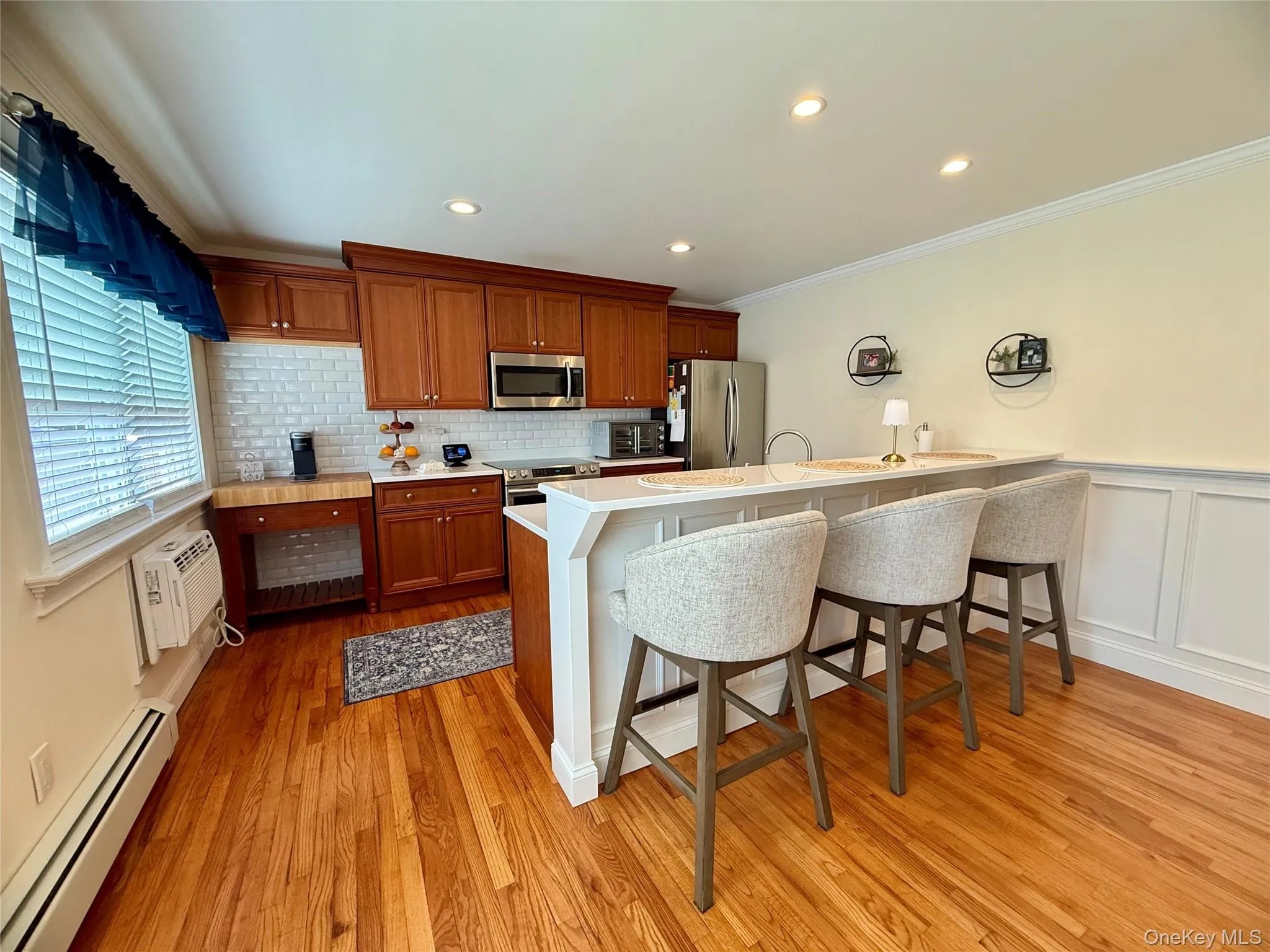 Kitchen featuring baseboard heating, appliances with stainless steel finishes, crown molding, and a breakfast bar area Kitchen featuring baseboard heating, appliances with stainless steel finishes, crown molding, and a breakfast bar area