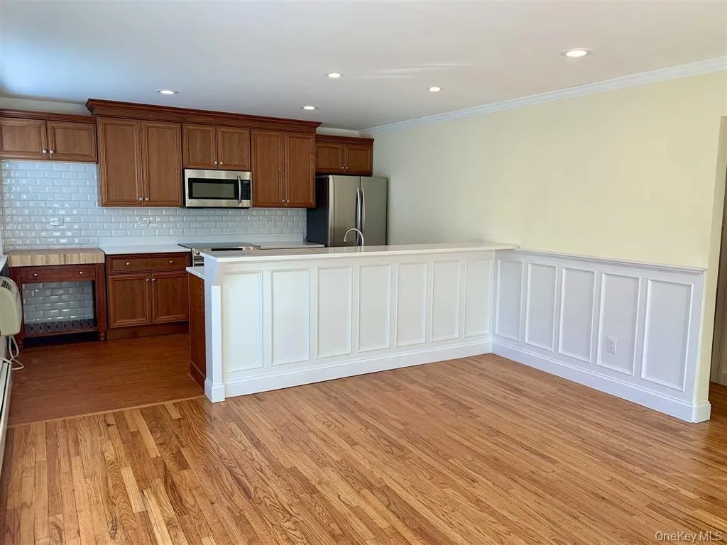 Kitchen featuring appliances with stainless steel finishes, brown cabinets, crown molding, light wood-style flooring, and light countertops Kitchen featuring appliances with stainless steel finishes, brown cabinets, crown molding, light wood-style flooring, and light countertops