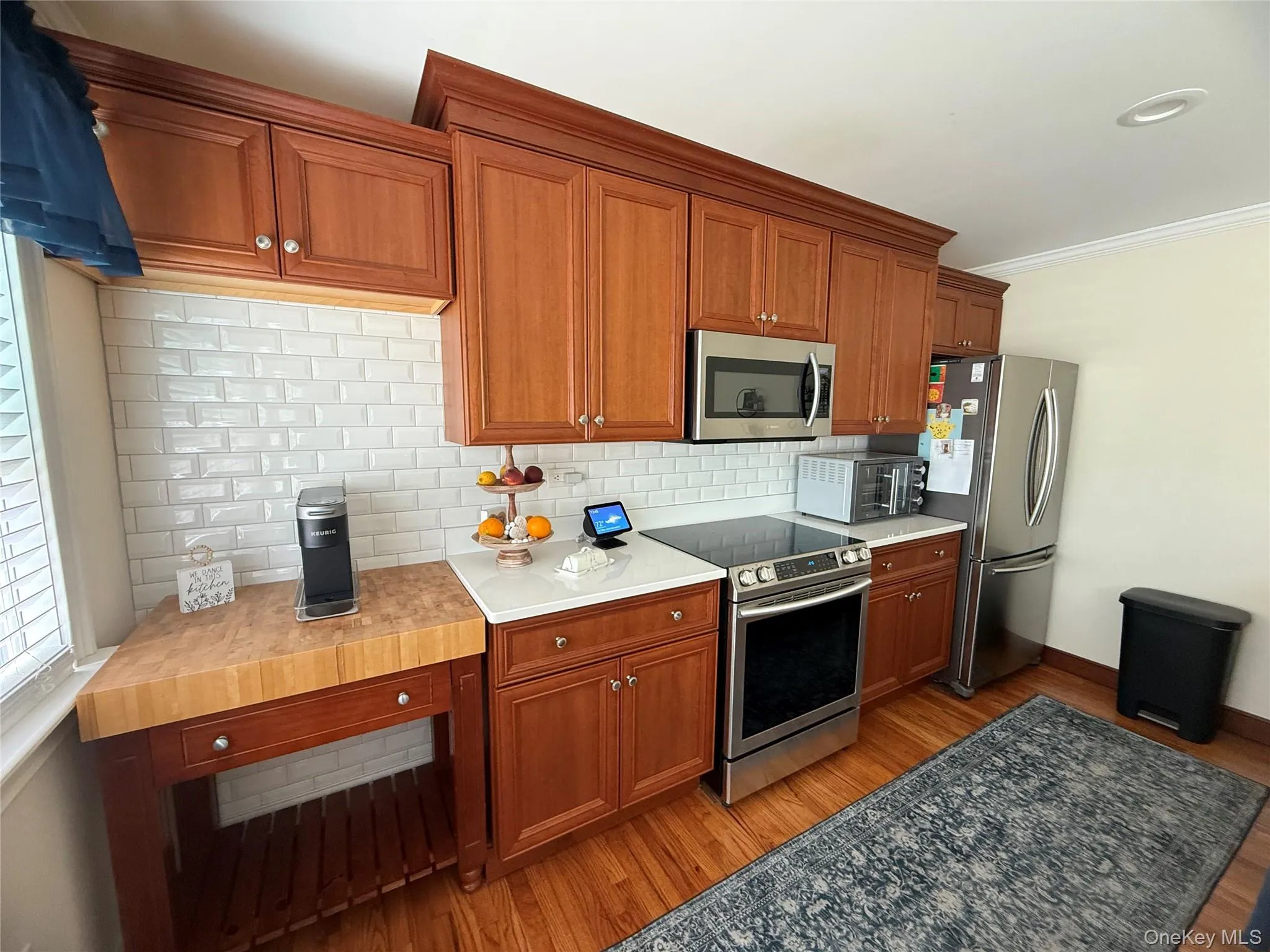 Kitchen featuring appliances with stainless steel finishes, light wood-style flooring, tasteful backsplash, brown cabinetry, and ornamental molding Kitchen featuring appliances with stainless steel finishes, light wood-style flooring, tasteful backsplash, brown cabinetry, and ornamental molding