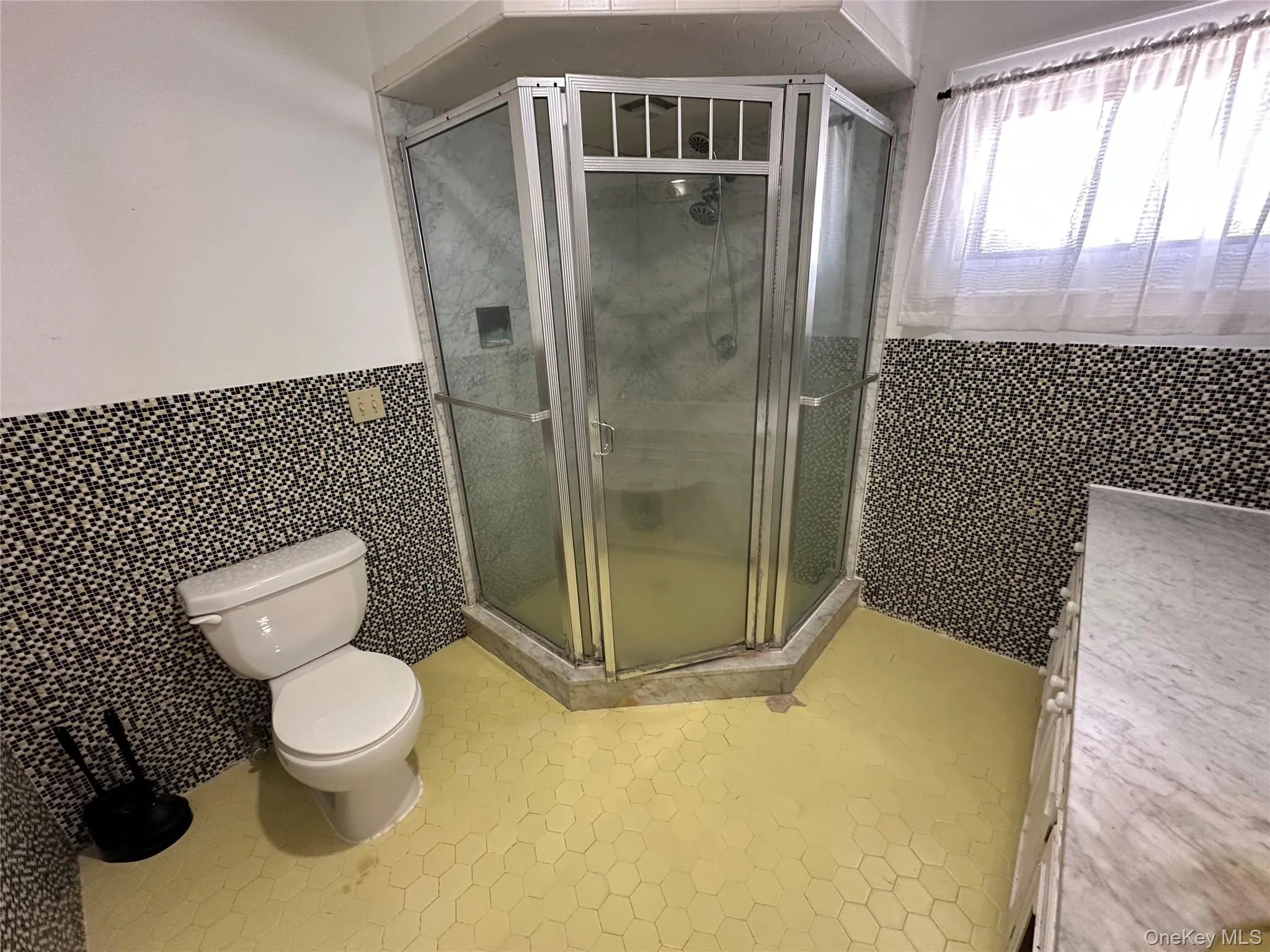 Full bath featuring a stall shower, toilet, a wainscoted wall, tile patterned flooring, and tile walls Full bath featuring a stall shower, toilet, a wainscoted wall, tile patterned flooring, and tile walls