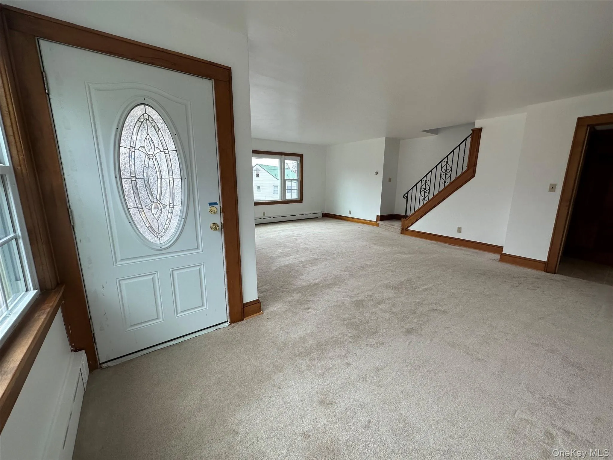 Entrance foyer featuring light carpet, a baseboard heating unit, stairway, and baseboards Entrance foyer featuring light carpet, a baseboard heating unit, stairway, and baseboards