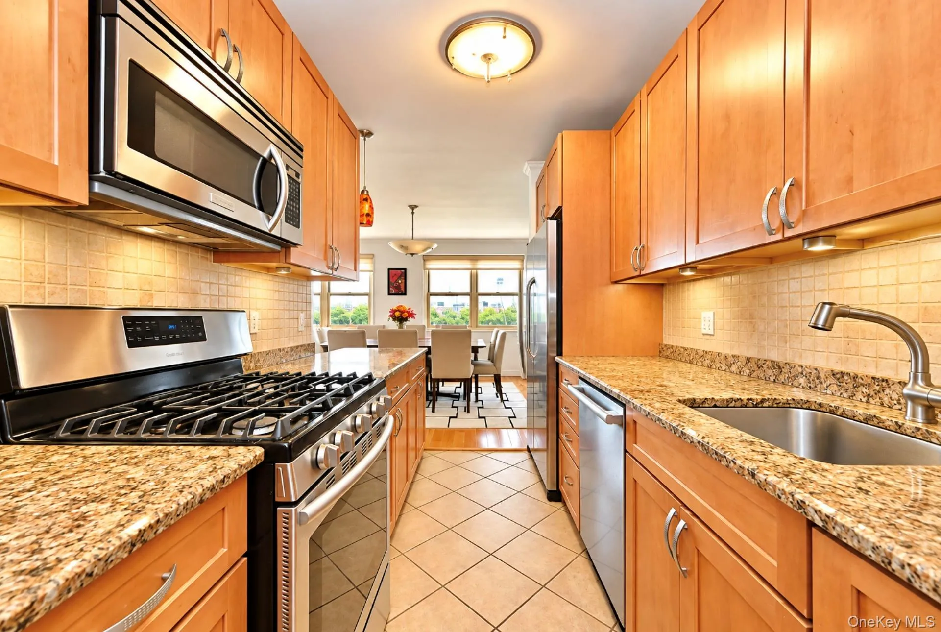 Galley kitchen featuring stainless steel appliances, light wood-finish cabinetry, granite countertops, and tiled flooring Galley kitchen featuring stainless steel appliances, light wood-finish cabinetry, granite countertops, and tiled flooring