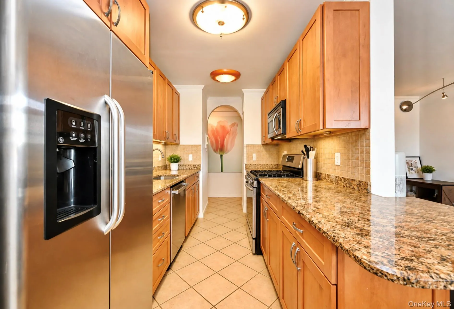 Galley kitchen featuring stainless steel appliances, wood cabinetry, granite countertops, and tile flooring Galley kitchen featuring stainless steel appliances, wood cabinetry, granite countertops, and tile flooring