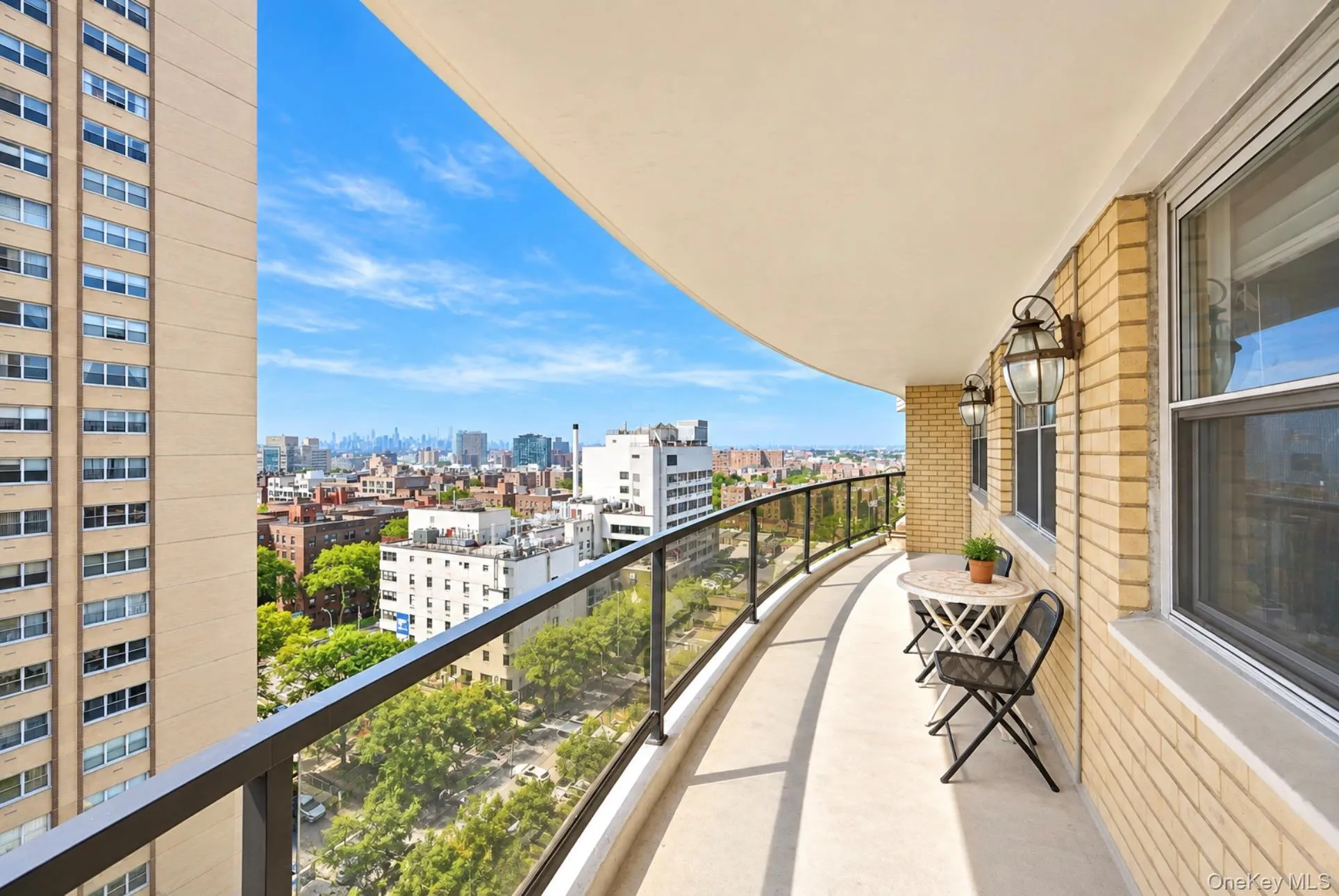 Expansive curved balcony featuring a glass and metal railing, concrete flooring, and brick exterior walls Expansive curved balcony featuring a glass and metal railing, concrete flooring, and brick exterior walls