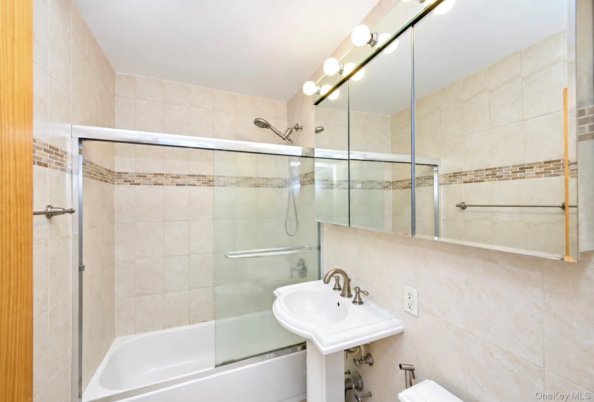 Pedestal sink with dual-handle faucet, mirrored medicine cabinet with integrated lighting, tiled shower and tub combination, and glass shower enclosure Pedestal sink with dual-handle faucet, mirrored medicine cabinet with integrated lighting, tiled shower and tub combination, and glass shower enclosure