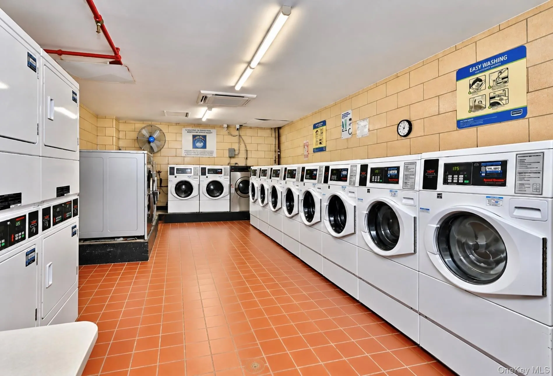 On-site laundry facility featuring multiple front-loading washers and dryers, a dedicated folding station, terra cotta tile flooring, and exposed brick walls On-site laundry facility featuring multiple front-loading washers and dryers, a dedicated folding station, terra cotta tile flooring, and exposed brick walls