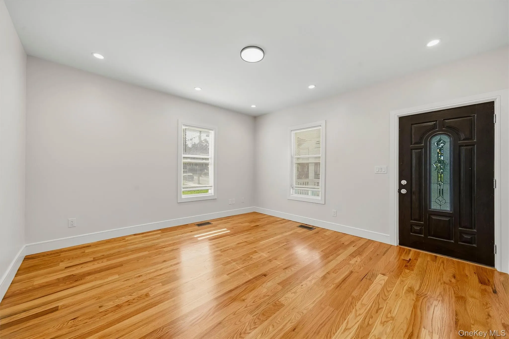 Hardwood-finish flooring, recessed lighting, and a dark wood entry door with stained glass accents Hardwood-finish flooring, recessed lighting, and a dark wood entry door with stained glass accents