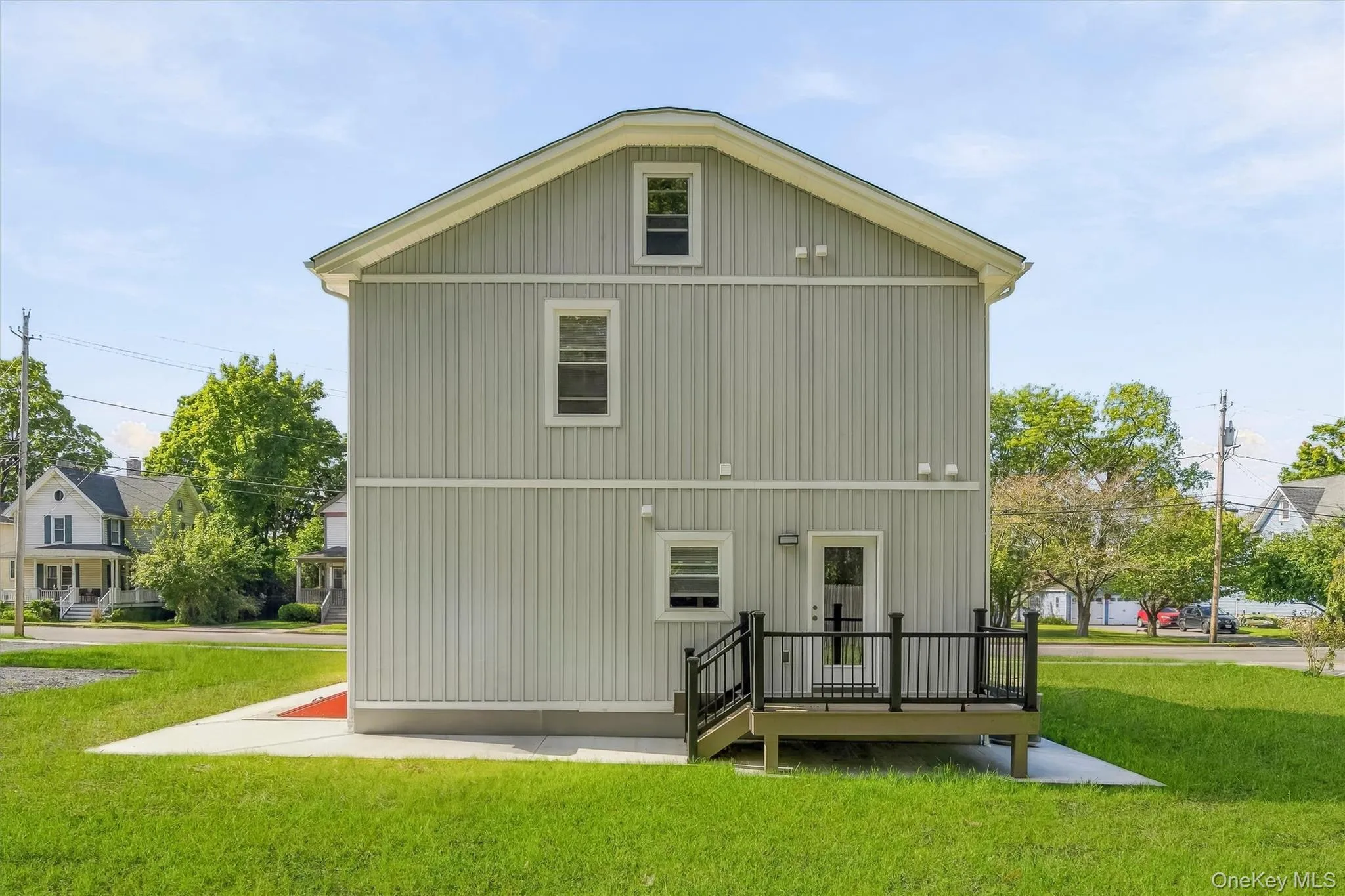 Light gray vertical siding exterior with white trim, a gabled roof, and a rear deck with black railings Light gray vertical siding exterior with white trim, a gabled roof, and a rear deck with black railings