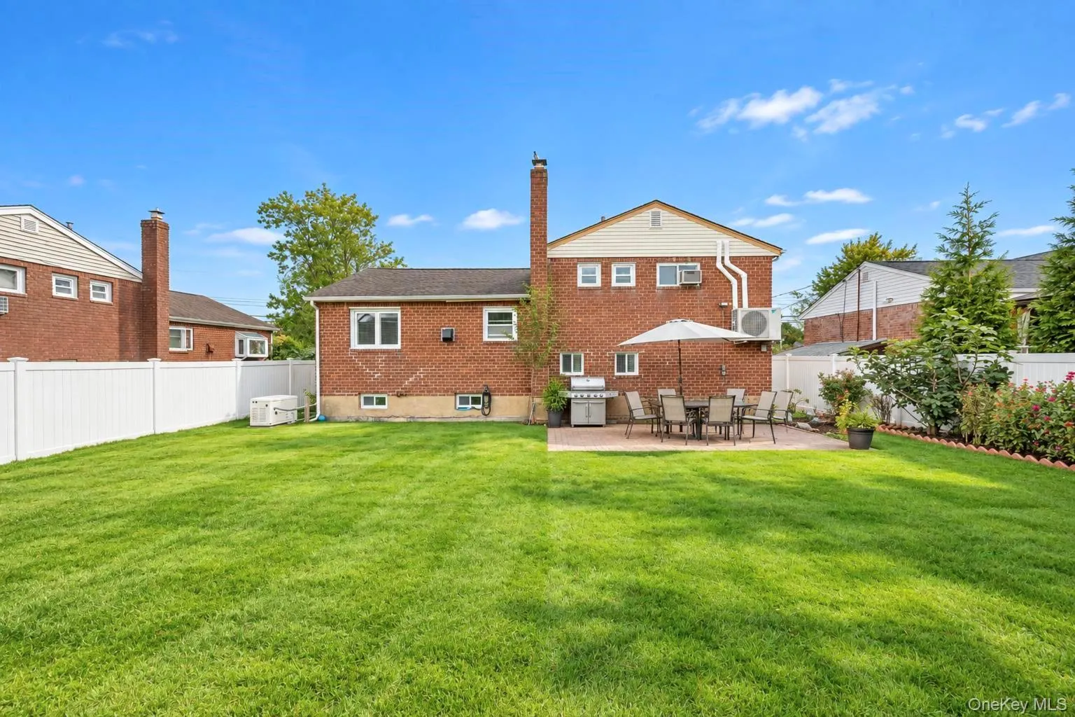 Expansive grassy yard with a paver patio, brick exterior, and white privacy fencing Expansive grassy yard with a paver patio, brick exterior, and white privacy fencing