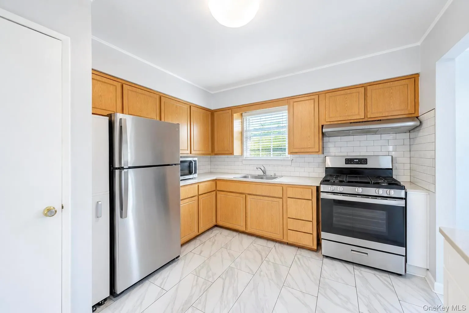 Kitchen featuring light wood cabinetry, stainless steel appliances, white subway tile backsplash, and white-finish flooring Kitchen featuring light wood cabinetry, stainless steel appliances, white subway tile backsplash, and white-finish flooring
