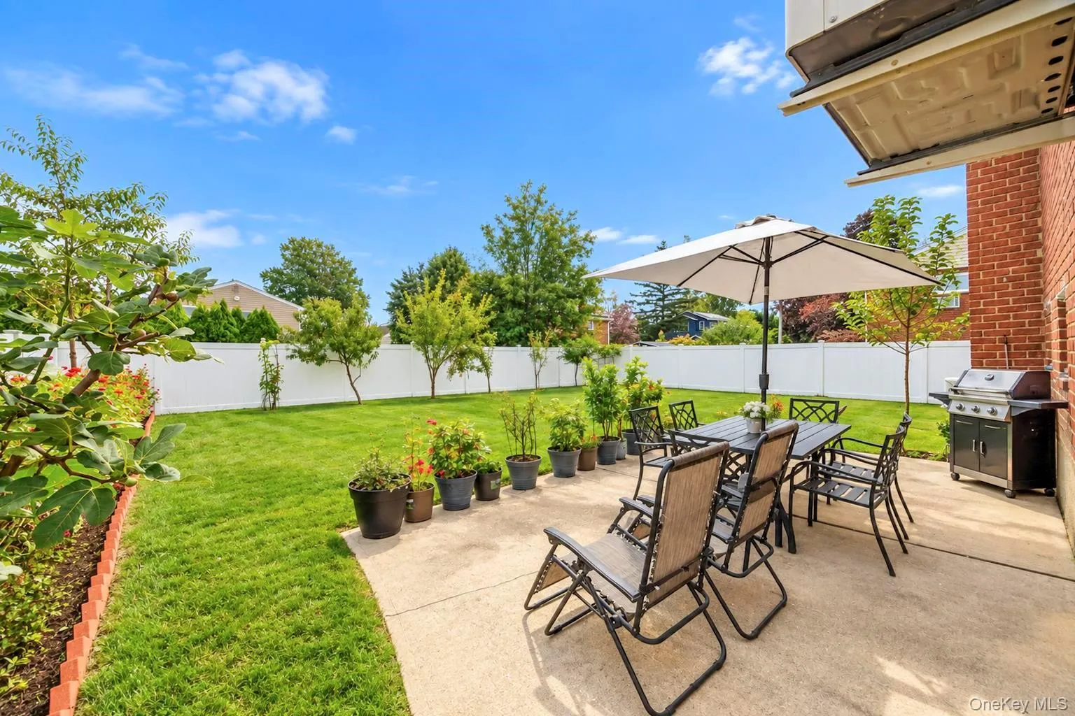 Expansive grass lawn with a white privacy fence, concrete patio, and a brick exterior Expansive grass lawn with a white privacy fence, concrete patio, and a brick exterior