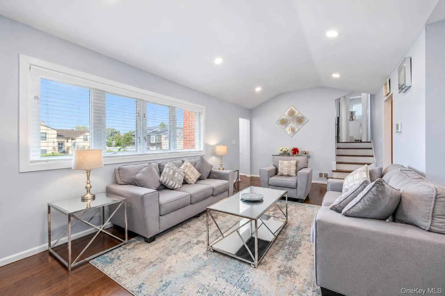 Hardwood-finish flooring, recessed ceiling lighting, vaulted ceiling, wide window with horizontal blinds, and a built-in staircase Hardwood-finish flooring, recessed ceiling lighting, vaulted ceiling, wide window with horizontal blinds, and a built-in staircase