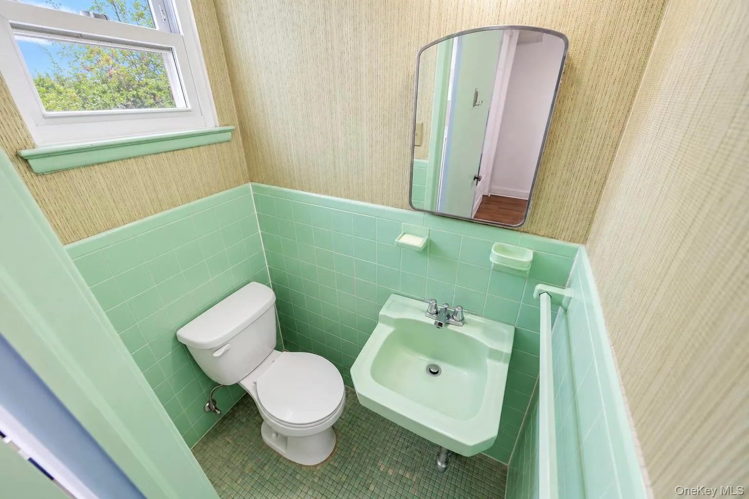 Green tiled walls, a white toilet, a matching green sink with a chrome faucet, and a wall-mounted mirror Green tiled walls, a white toilet, a matching green sink with a chrome faucet, and a wall-mounted mirror