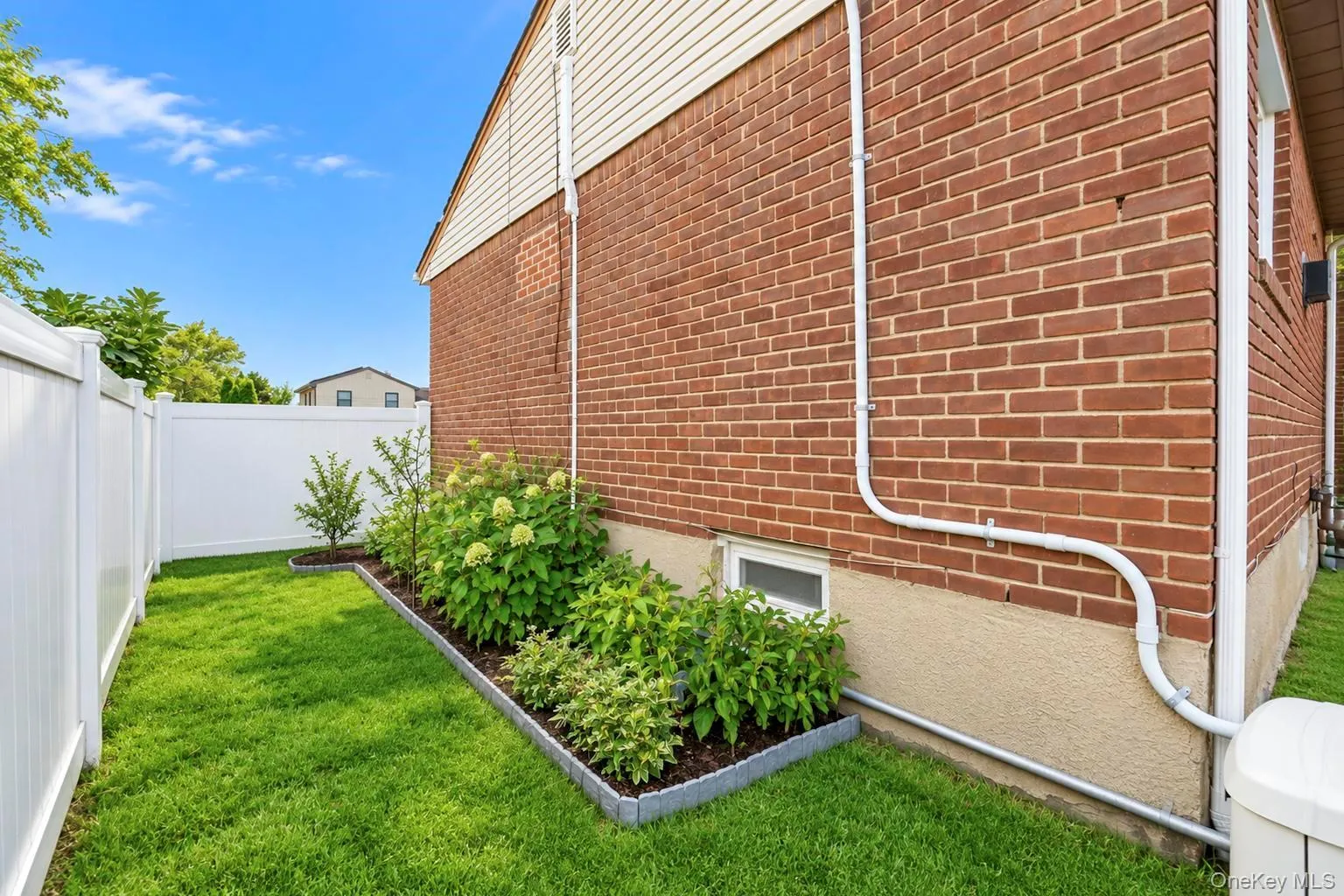 Manicured lawn with mature landscaping, brick exterior, and white privacy fencing Manicured lawn with mature landscaping, brick exterior, and white privacy fencing