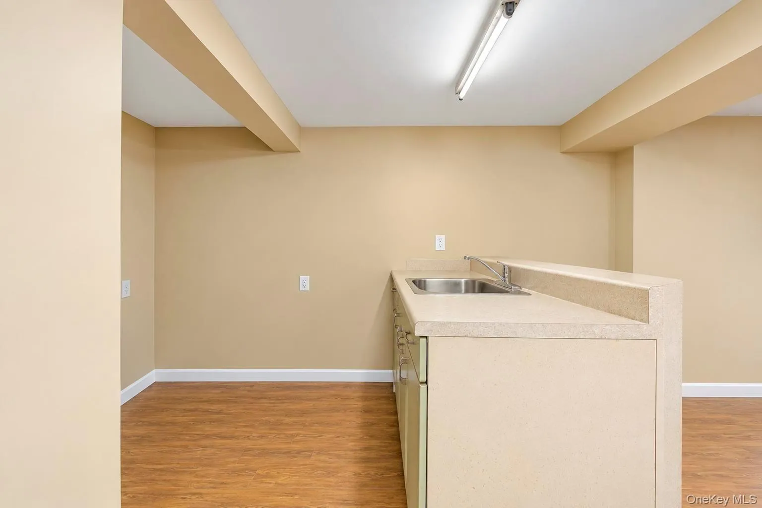 Kitchenette with a dual-basin stainless steel sink, light-toned countertop, and wood-finish flooring Kitchenette with a dual-basin stainless steel sink, light-toned countertop, and wood-finish flooring