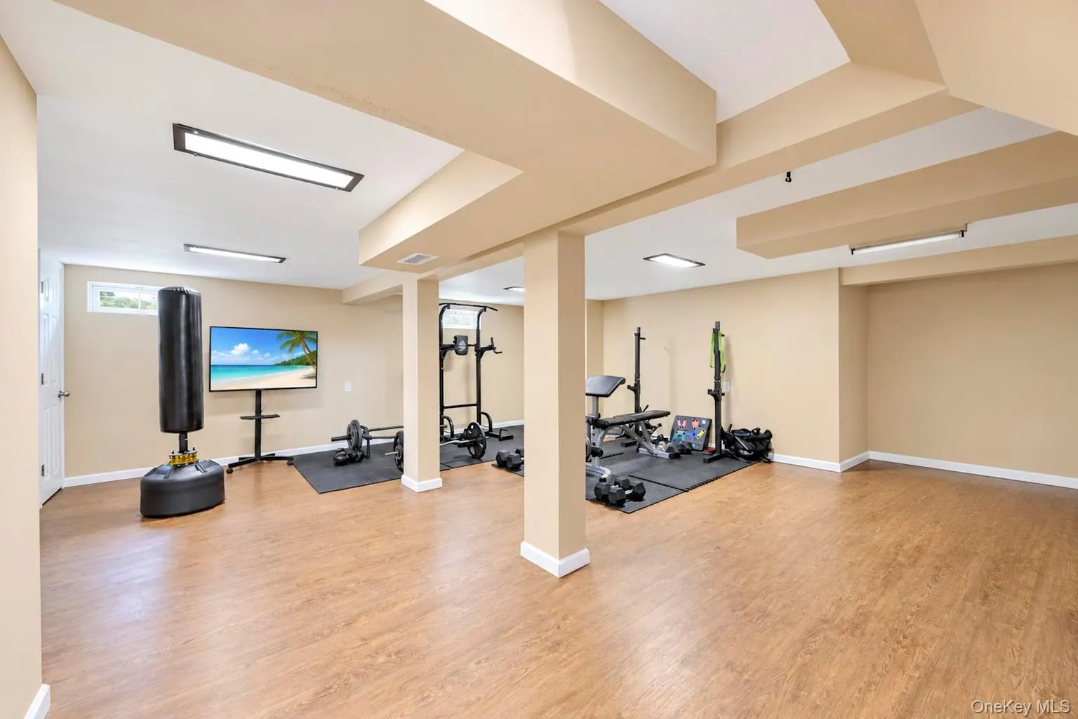 Expansive recreation area with wood-finish flooring, recessed lighting, and structural columns Expansive recreation area with wood-finish flooring, recessed lighting, and structural columns
