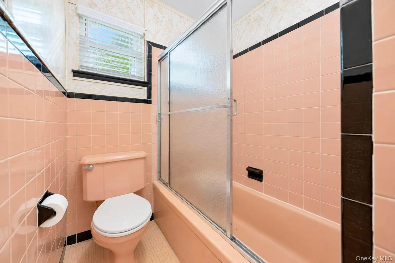 Bathroom with peach ceramic wall tiling, black accent tile, and a built-in bathtub with a sliding glass enclosure Bathroom with peach ceramic wall tiling, black accent tile, and a built-in bathtub with a sliding glass enclosure