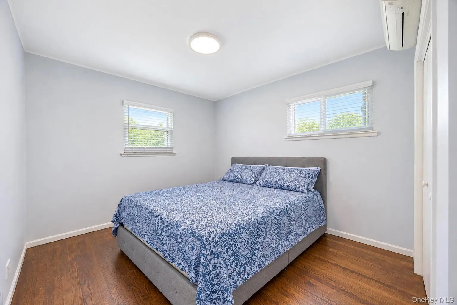 Hardwood flooring, two windows with blinds, recessed lighting, and a wall-mounted air conditioning unit Hardwood flooring, two windows with blinds, recessed lighting, and a wall-mounted air conditioning unit