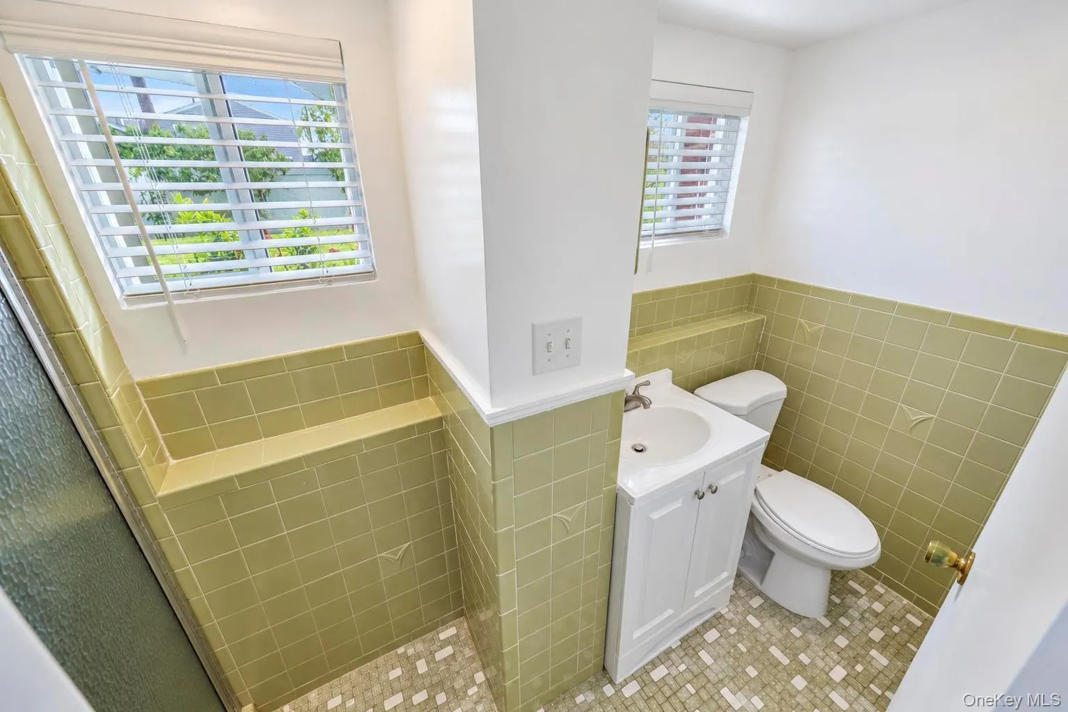 Bathroom featuring mosaic tile flooring, a single vanity with storage, and a built-in shower ledge Bathroom featuring mosaic tile flooring, a single vanity with storage, and a built-in shower ledge