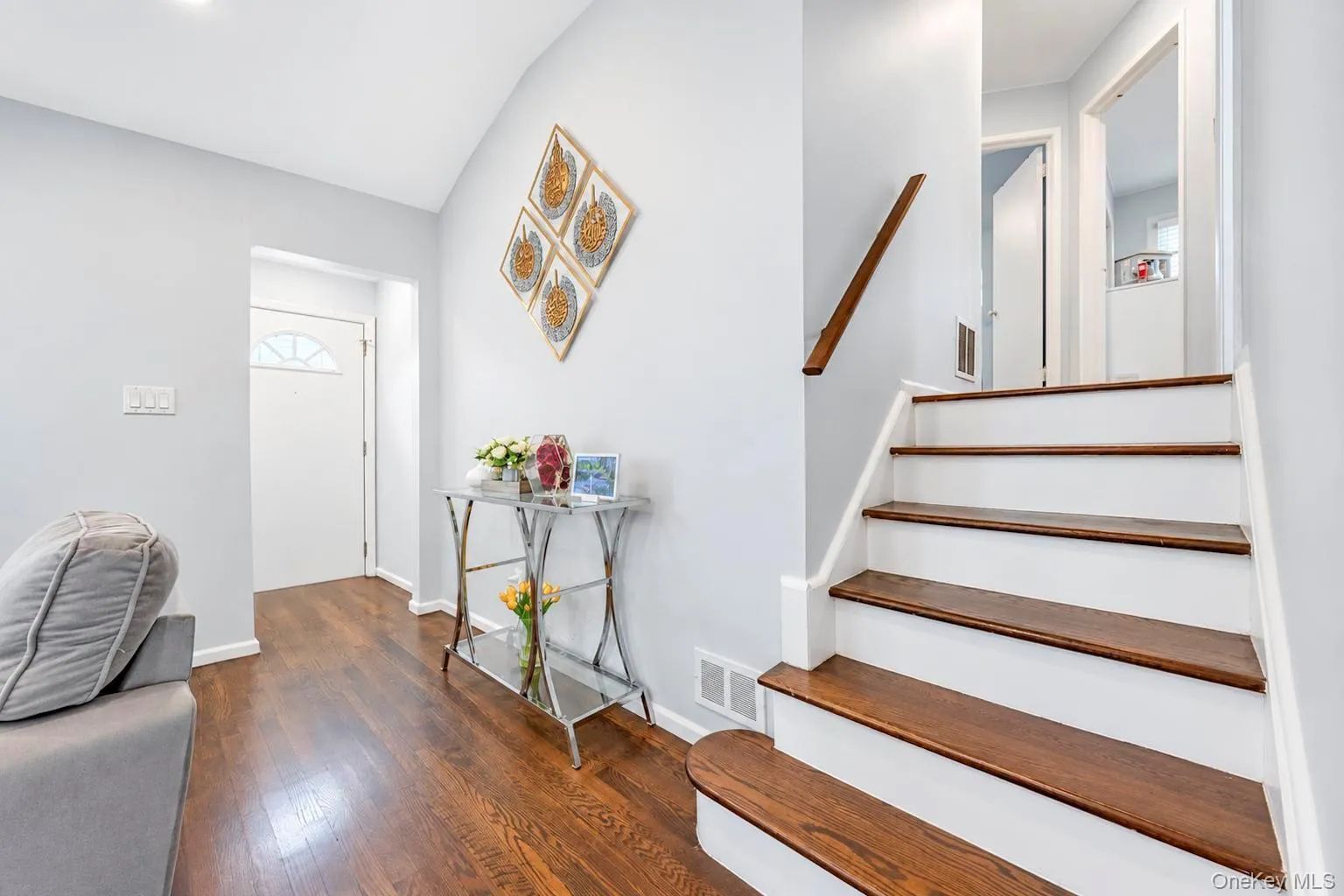 Wood-finish flooring extending into the entry, white painted walls, and a staircase with wood-finish treads and a wood handrail Wood-finish flooring extending into the entry, white painted walls, and a staircase with wood-finish treads and a wood handrail