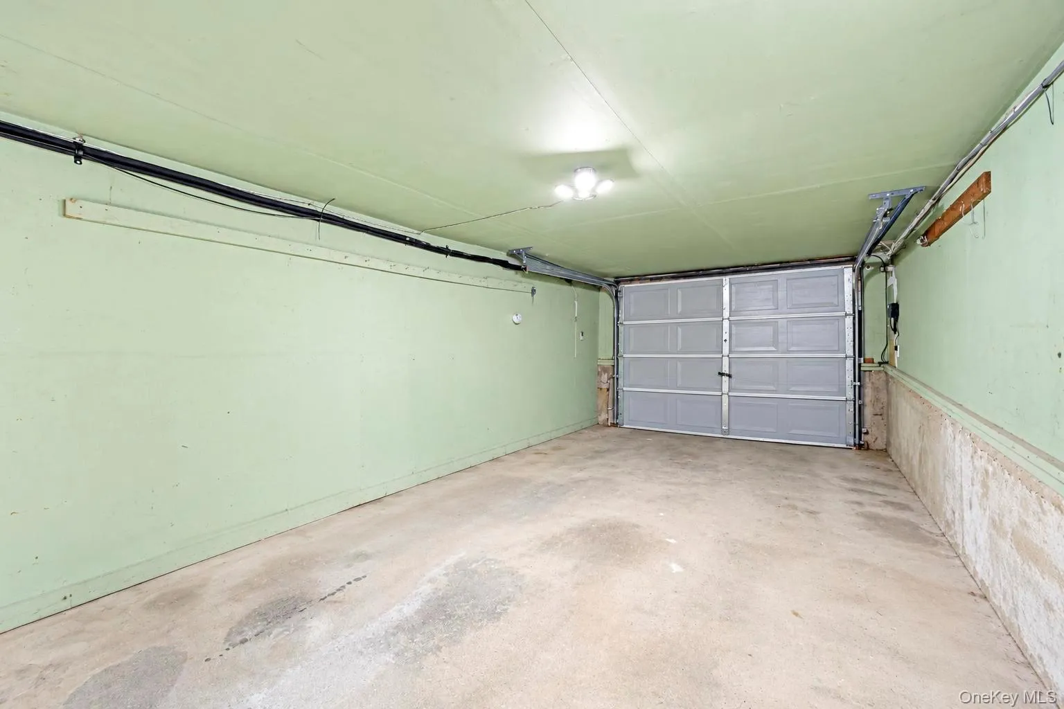 Attached garage with concrete flooring, overhead lighting, and a paneled garage door Attached garage with concrete flooring, overhead lighting, and a paneled garage door