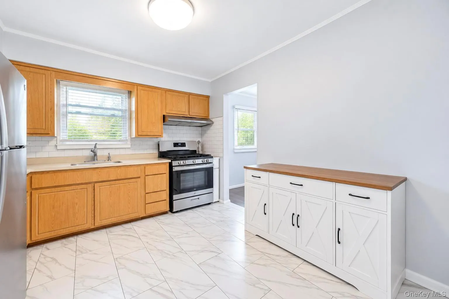 Kitchen featuring light wood cabinetry, a stainless steel range, a white subway tile backsplash, and light-toned tile flooring Kitchen featuring light wood cabinetry, a stainless steel range, a white subway tile backsplash, and light-toned tile flooring