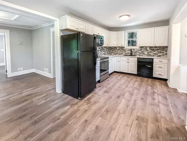 Kitchen featuring white cabinetry, dark appliances, patterned tile backsplash, and wood-finish flooring Kitchen featuring white cabinetry, dark appliances, patterned tile backsplash, and wood-finish flooring