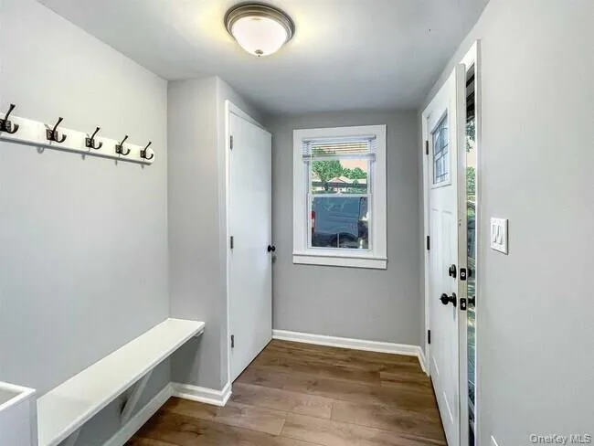 Entryway featuring wood-finish flooring, a flush-mount ceiling light, built-in coat hooks, and a built-in bench Entryway featuring wood-finish flooring, a flush-mount ceiling light, built-in coat hooks, and a built-in bench