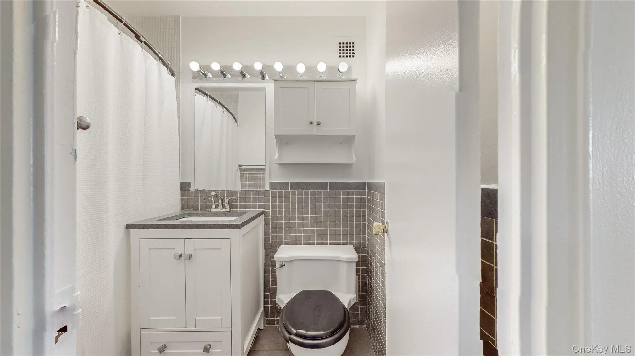 White vanity with under-sink storage, a single basin sink, and a dark-toned countertop White vanity with under-sink storage, a single basin sink, and a dark-toned countertop