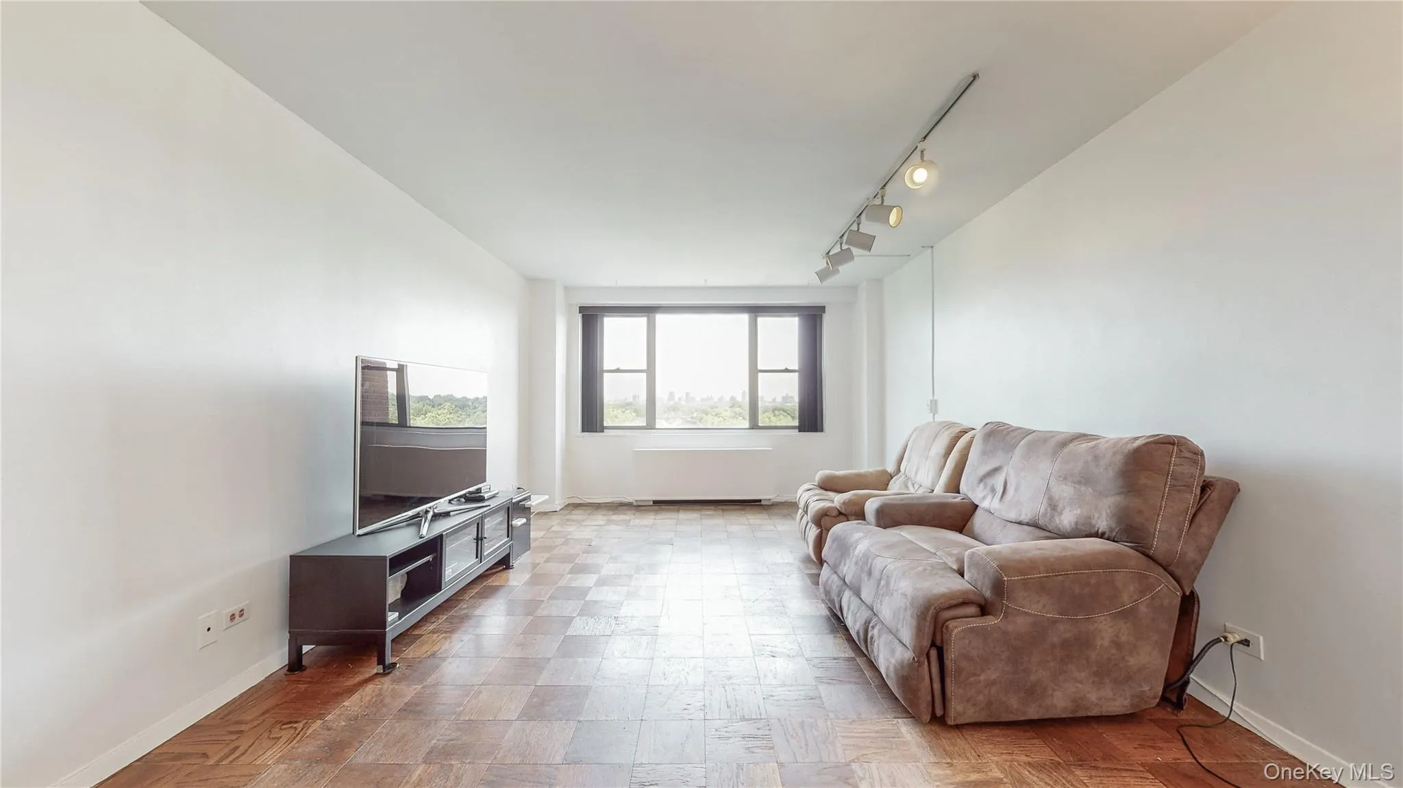 Wood-finish parquet flooring throughout, expansive white walls, track lighting fixture, and large windows Wood-finish parquet flooring throughout, expansive white walls, track lighting fixture, and large windows