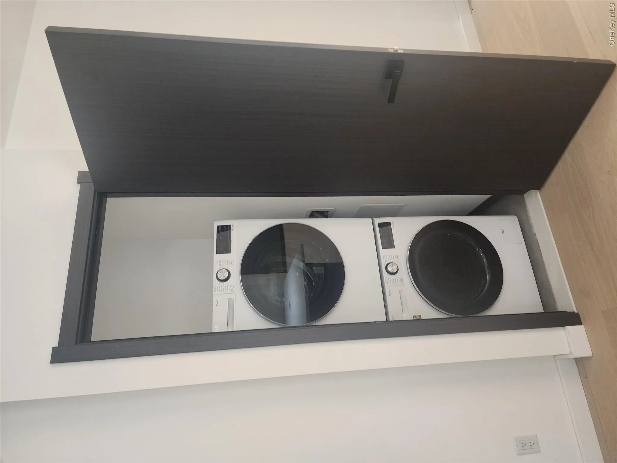 Built-in laundry closet with stacked washer and dryer, finished with a dark wood-finish door and frame, set against light wood-finish flooring Built-in laundry closet with stacked washer and dryer, finished with a dark wood-finish door and frame, set against light wood-finish flooring