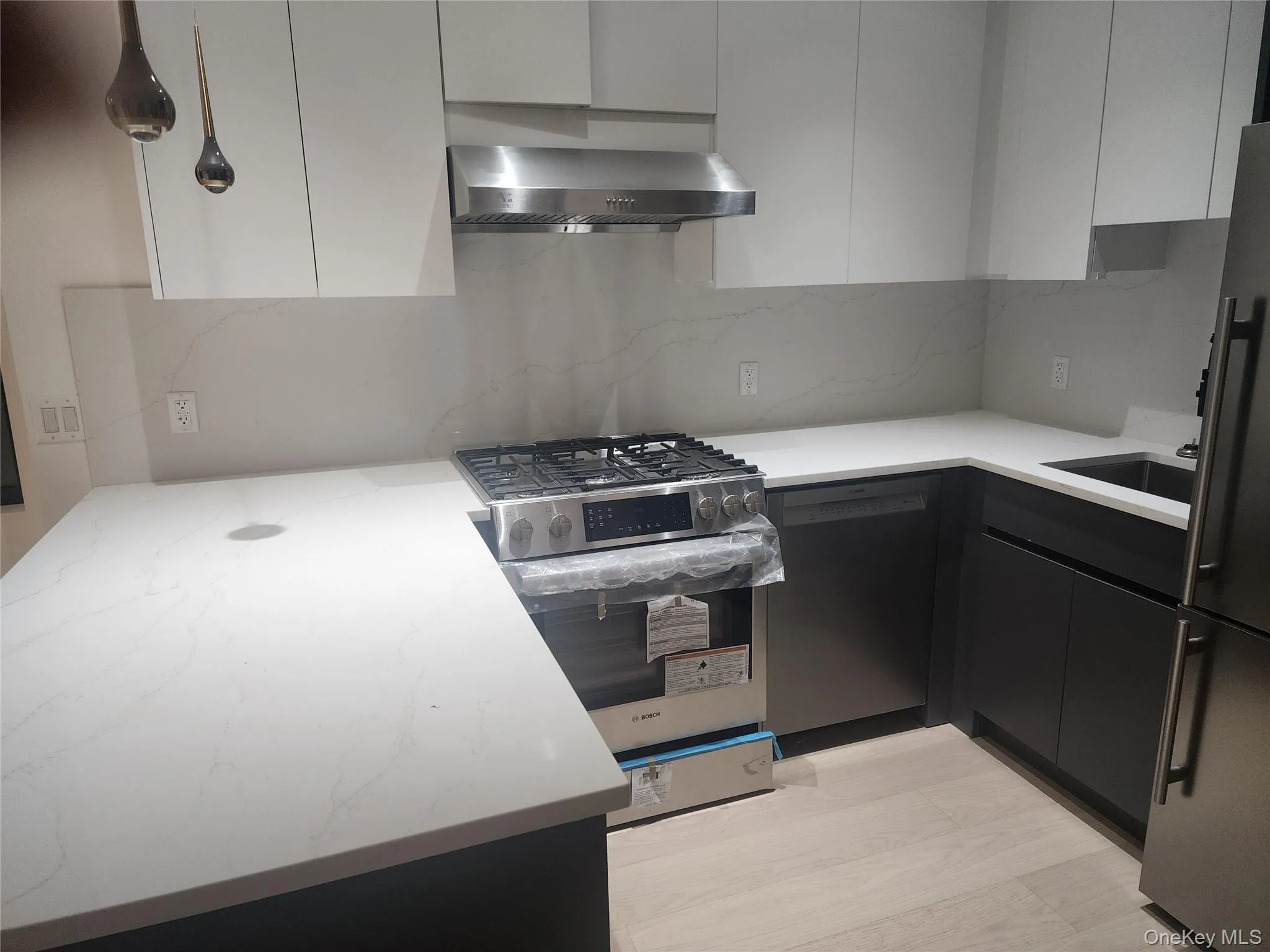 Modern kitchen featuring light wood-finish flooring, white countertops, white upper cabinetry, dark lower cabinetry, and stainless steel appliances Modern kitchen featuring light wood-finish flooring, white countertops, white upper cabinetry, dark lower cabinetry, and stainless steel appliances