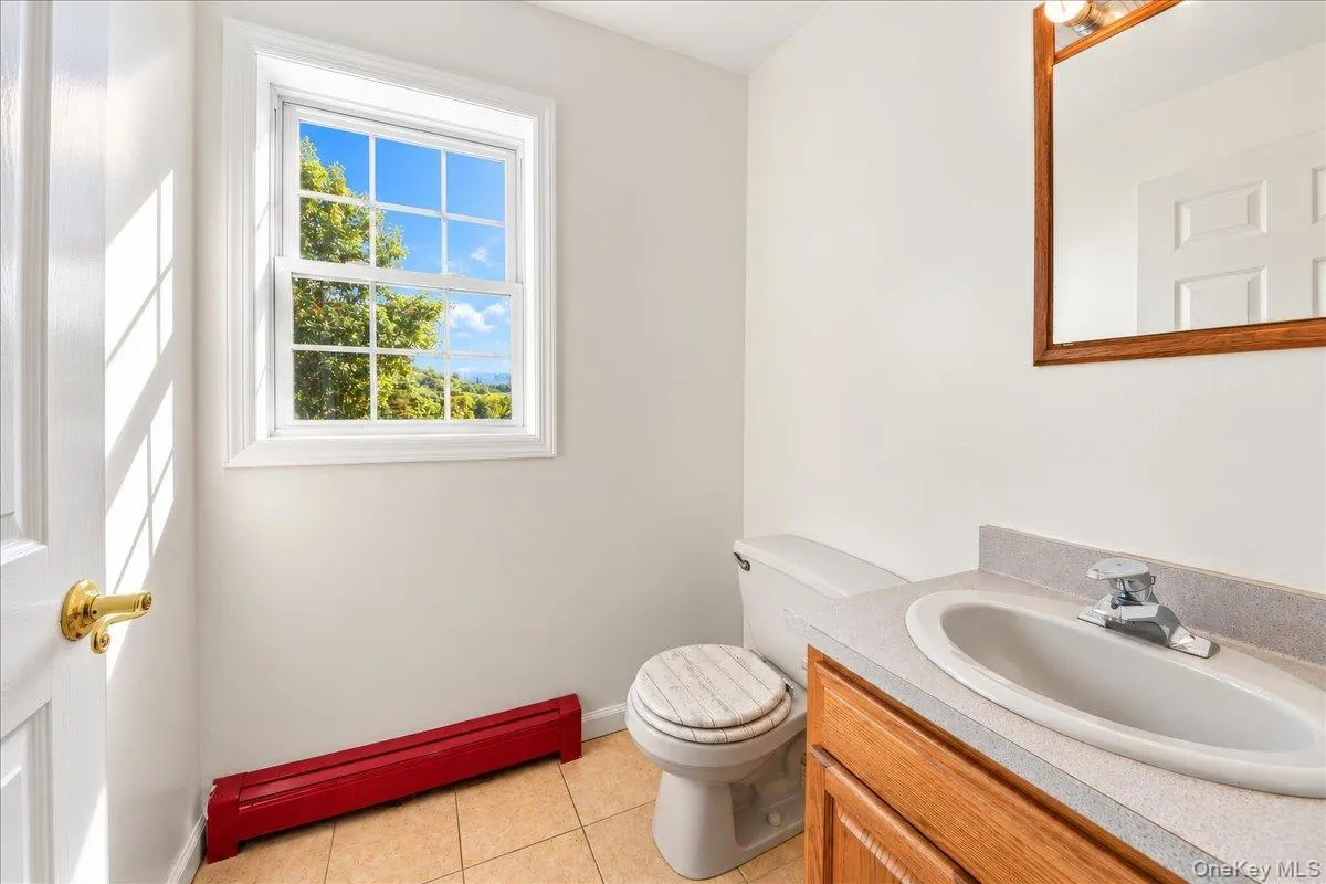 Single-hung window, ceramic tile flooring, wood-finish vanity, light-colored countertop, and a wood-framed mirror Single-hung window, ceramic tile flooring, wood-finish vanity, light-colored countertop, and a wood-framed mirror