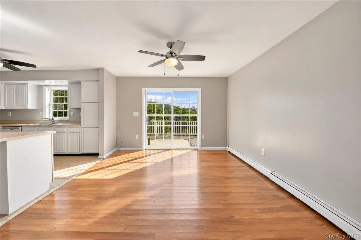 Open-concept living area featuring wood-finish flooring, a ceiling fan, and access to an outdoor deck through a glass sliding door Open-concept living area featuring wood-finish flooring, a ceiling fan, and access to an outdoor deck through a glass sliding door